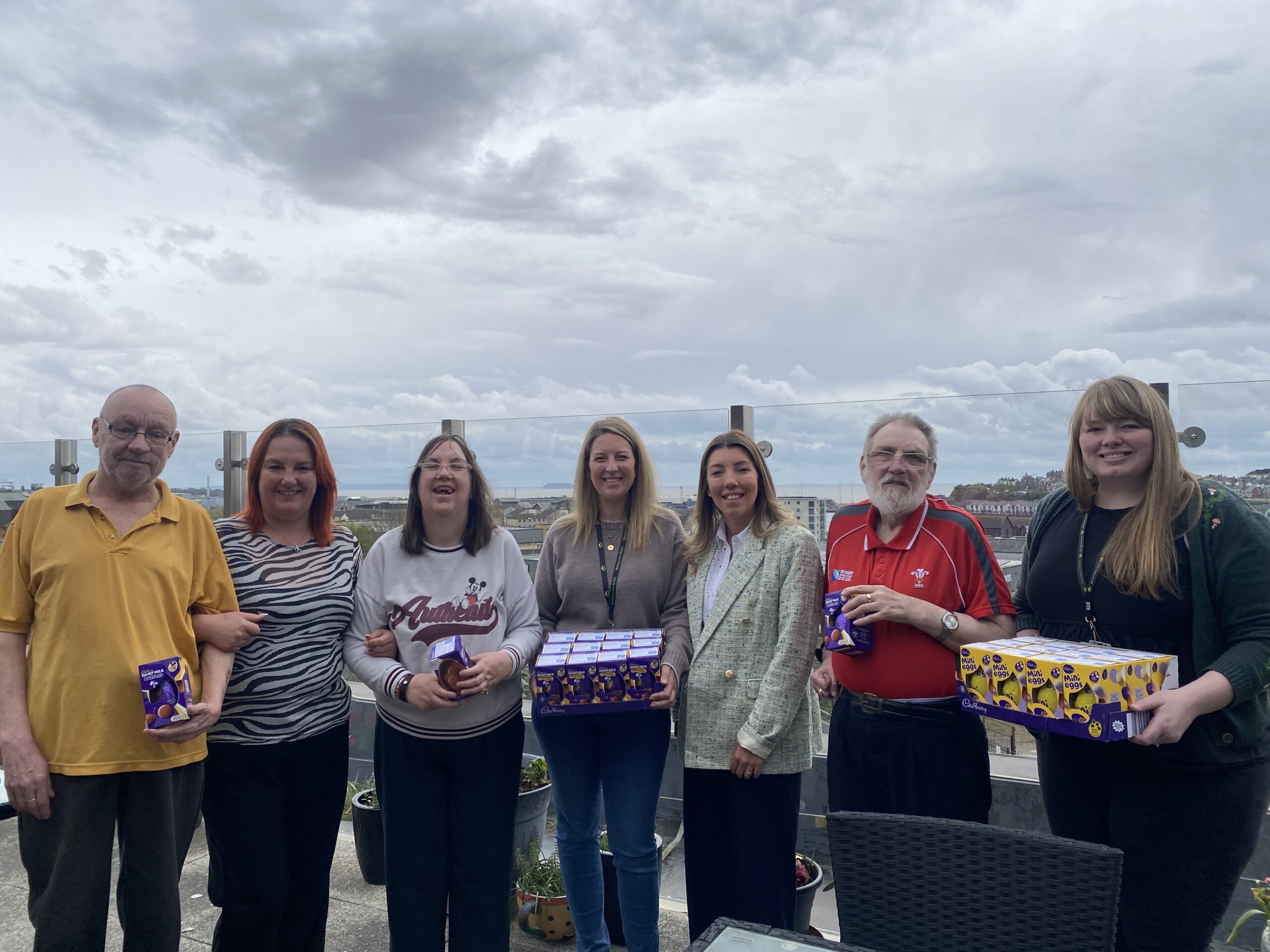 Seven people smiling and holding easter eggs against skyline backdrop