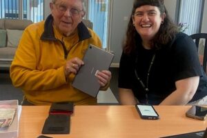 Two people sat at a table with laptop and phones