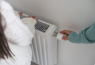 warming hands on heating radiator near white wall
