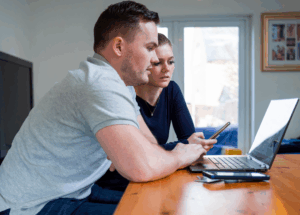 two people looking at a laptop and a smart phone in their home